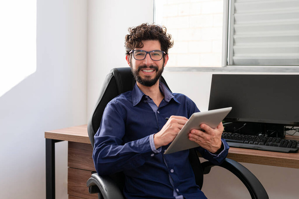 Homme d'affaires dans son bureau à l'aide d'une tablette regardant la caméra sourire. Concept bureau à domicile. - Photo, image