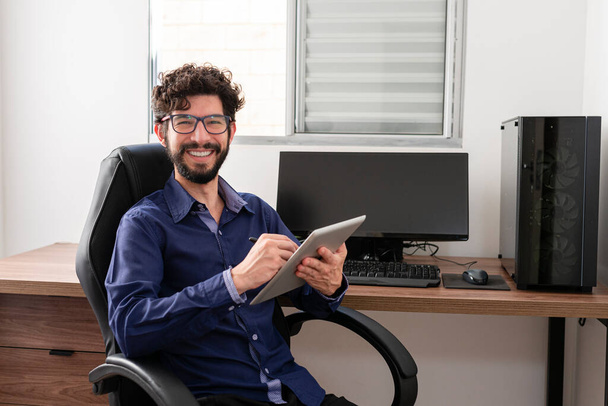 Hispanic man in his office using tablet looking at camera smiling. Home office concept. - Foto, Bild