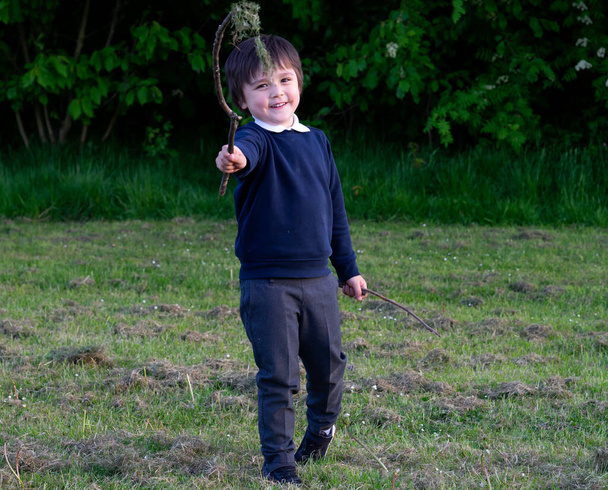 Roztomilý malý kluk hrající si s dřevěnou holí na zahradě, školačka drží dřevěnou hůl s trávou v parku, aktivní dítě hraje venku v létě. - Fotografie, Obrázek