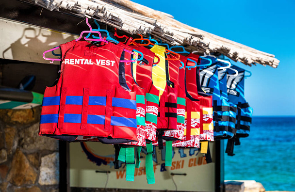 The group of colourfull life jackets or life vests or air jackets hanging on hanger on the row. Sea and sky at the background. - Photo, Image