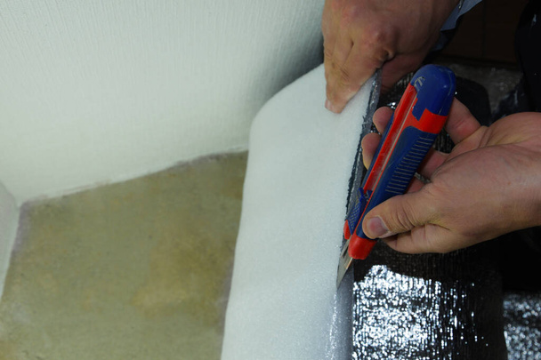 Чоловік ремонтує квартиру, роблячи утеплення підлоги утепленням з фольги. Рука вирізає фольгу для щільного укладання її на підлогу
. - Фото, зображення