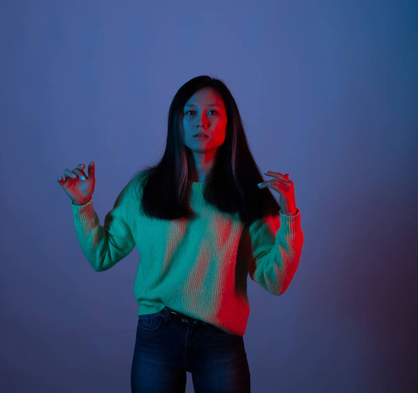 Pretty young woman looking at the camera is gesturing in blue and red light over violet background - 写真・画像