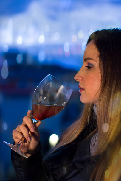 Young woman relaxing and drinking a glass of red wine at home at sunset in the evening - Foto, Imagen