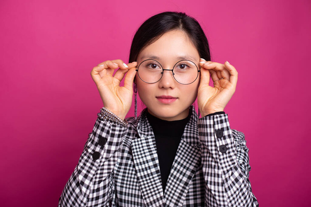 Charming girl wearing glasses and suit jacket is looking at the camera over pink background - Foto, immagini