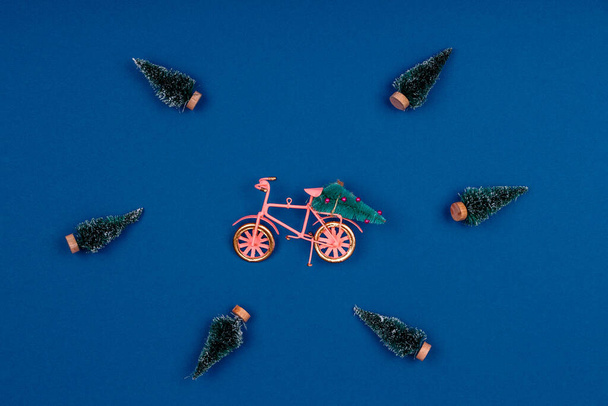 Fahrrad mit Weihnachtsbaum umgeben von verschneiten Bäumen auf klassischem Blau - Foto, Bild