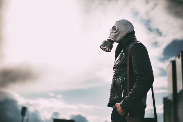 casual young man in a gas mask standing on the street in an empty city - Foto, afbeelding
