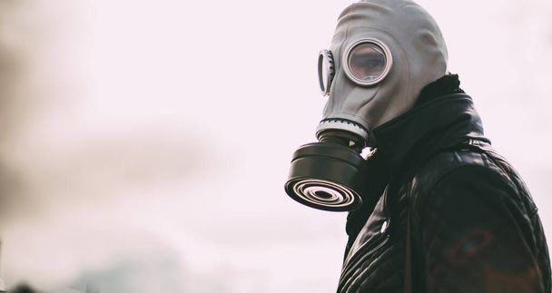 Boş bir şehirde sokakta duran gaz maskeli sıradan bir genç adam. - Fotoğraf, Görsel
