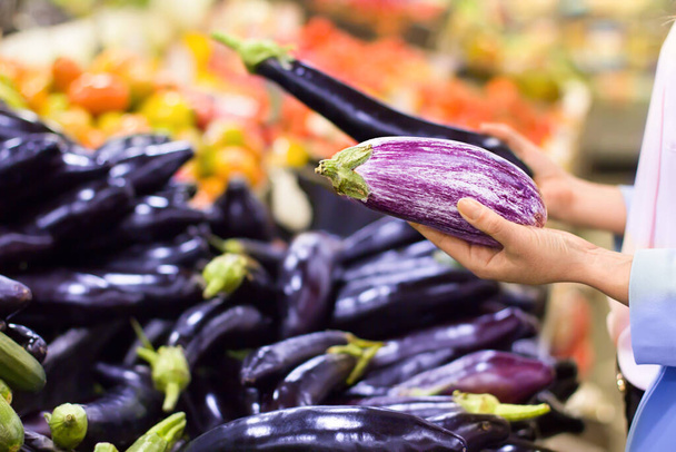 Mão feminina escolhendo berinjela no supermercado. Conceito de comida saudável, bio, vegetariano, dieta
. - Foto, Imagem
