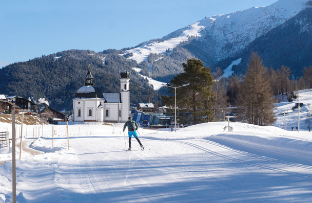 Avusturya 'nın tipik pitoresk kilisesi Seefeld, Avusturya' ya doğru güneşli pistte kros kayakçısı - Fotoğraf, Görsel