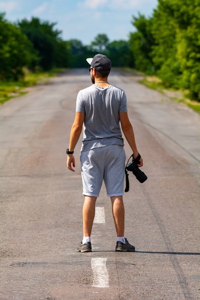Genç bir fotoğrafçı yolda duruyor ve uzaklığa bakıyor. - Fotoğraf, Görsel