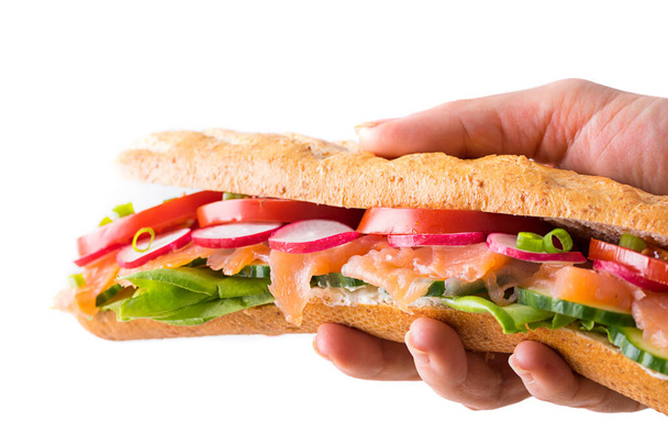 Mão segurando sanduíches submarinos frescos com recheio de queijo macio, salmão, alface, pepino, rabanete, tomate e cebolinha. Fous no meio
 - Foto, Imagem