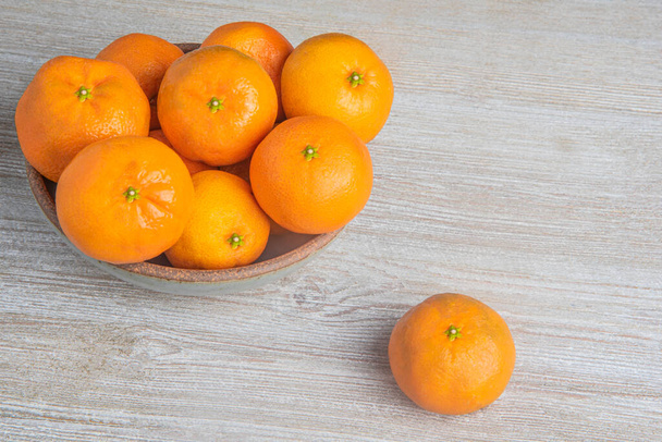 Un ramo de naranjas frescas en un cuenco de cerámica sobre un tablero de madera texturizada pintada de blanco
. - Foto, Imagen