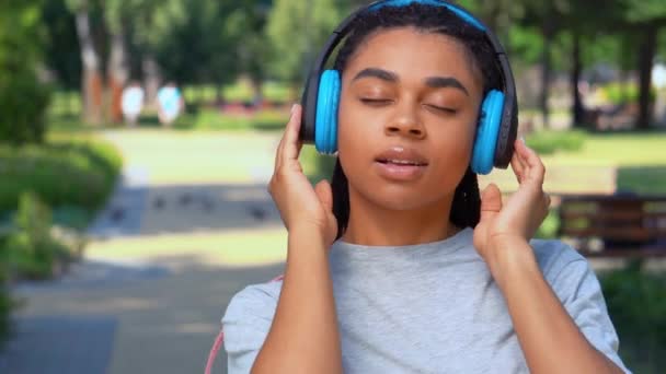 Gesicht Mixed Race Frau mit Kopfhörer suchen Kamera im Park - Filmmaterial, Video