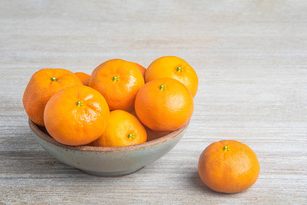 Hromada čerstvých pomerančů v keramické misce na bíle natřené dřevěné desce. - Fotografie, Obrázek