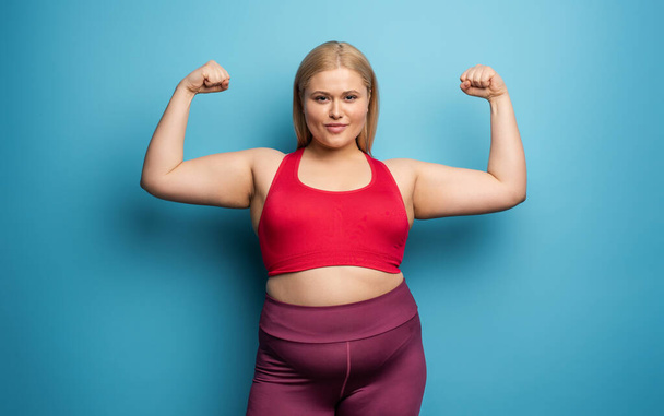 Fat girl does gym at home. satisfied expression. Cyan background - Фото, изображение