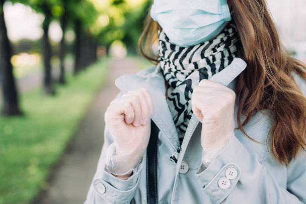 Kaukasisches Mädchen mit medizinischer Maske und grauem Mantel spaziert durch den Park. - Foto, Bild