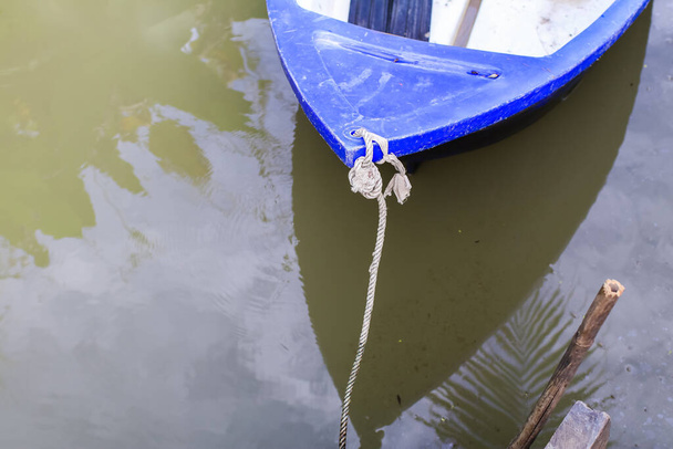 古い木製のドックに接続された水の上に小さな青いプラスチック製のボート. - 写真・画像