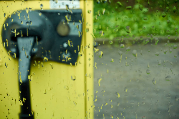 Aspirateur jaune, dans le parking, avec une machine à sous Euro coin, photographié à travers le panneau de fenêtre de pluie, profondeur de champ, Allemagne. - Photo, image