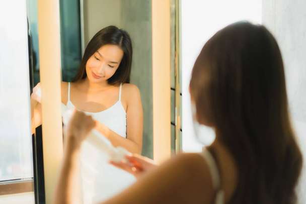 Πορτρέτο όμορφη νεαρή Ασιάτισσα γυναίκα καθαρίσει το πρόσωπο και το πρόσωπό της με καθρέφτη στο εσωτερικό του μπάνιου - Φωτογραφία, εικόνα