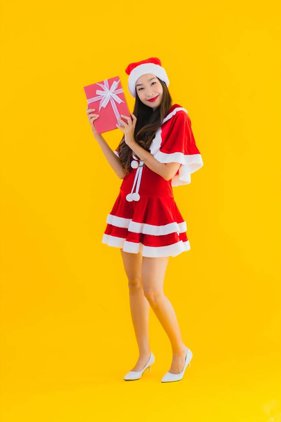 Portrait beautiful young asian christmas clothes and hat smile happy with red gift box on yellow isolated background - Photo, image