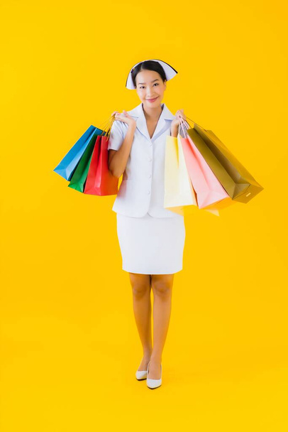 Portrait beautiful young asian woman thai nurse with shopping bag and credit card on yellow isolated background - Photo, image