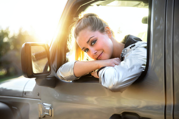 Cute fun flirty smile from beautiful blonde woman outdoors driving in a car through nature, adventure and freedom in automobile - Photo, Image