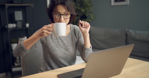 Happy woman drinking coffee and watching movie on laptop - Imágenes, Vídeo