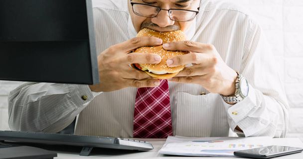 Οι εργαζόμενοι άνδρες δεν έχουν χρόνο για επείγουσα κατανάλωση junk food hamburger ενώ εργάζονται στο γραφείο - Φωτογραφία, εικόνα