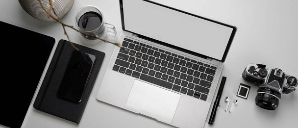 Вид сверху на современное рабочее пространство с макетом ноутбука, фотоаппаратом, планшетом, канцелярскими принадлежностями, чашкой кофе и украшением
 - Фото, изображение