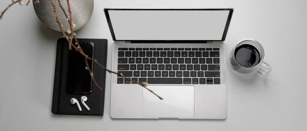 Κάτοψη του απλού μοντέρνου χώρου εργασίας με mock-up laptop, ασύρματο ακουστικό, βιβλίο χρονοδιαγράμματος, φλιτζάνι καφέ και βάζο - Φωτογραφία, εικόνα