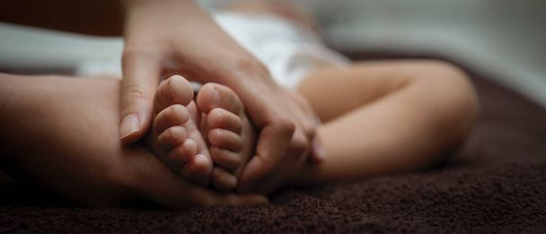 Close up view of parent hands holding tiny feet newborn baby on bed - Fotoğraf, Görsel