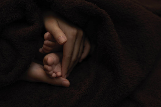 Anne elleri yeni doğmuş bebek ayaklarını koyu arka planda tutuyor - Fotoğraf, Görsel