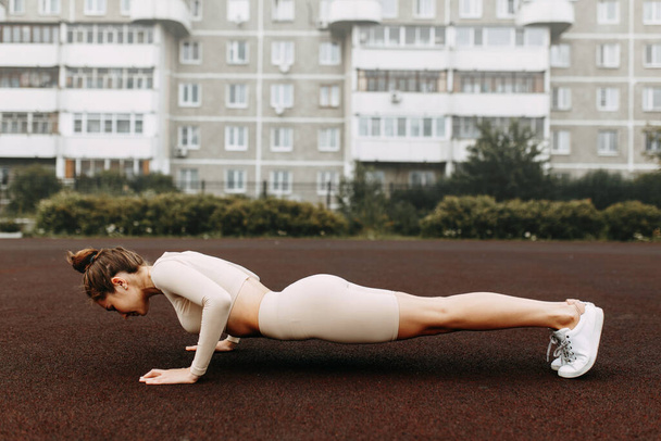 A sporty woman trains and exercises at a fitness stadium. Warm-up in the open air, stretching. - Foto, Imagen
