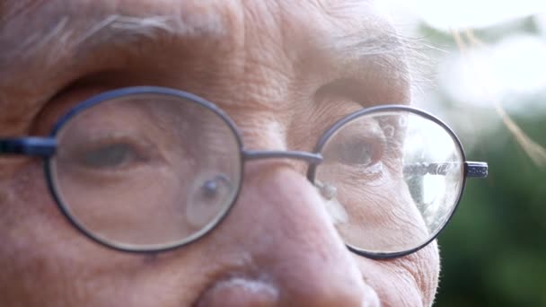Detailní záběr očí staršího muže s brýlemi, který sedí nepřítomný ve slunné zahradě s přirozeným pozadím bokeh. selektivní zaměření. - Záběry, video