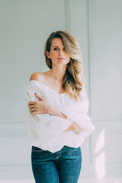 Beautiful elegant sexy girl in a white blouse with magnificent sleeves and flared jeans in a room filled with the sun. Beauty and fashion style. Soft selective focus. - Foto, imagen
