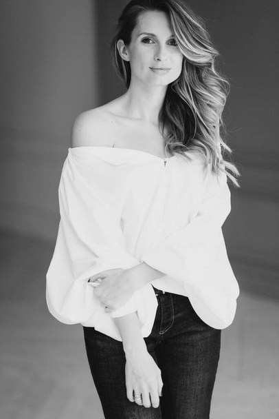 Menina sexy elegante bonita em uma blusa branca com mangas magníficas e jeans queimados no quarto. Beleza e estilo de moda. Foco seletivo suave
. - Foto, Imagem