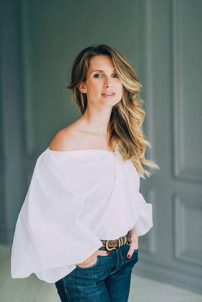 Beautiful elegant sexy girl in a white blouse with magnificent sleeves and flared jeans in the room. Beauty and fashion style. Soft selective focus. - Foto, immagini