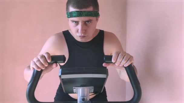 Cheerful fat man in a funny tracksuit is engaged in a stationary bike. The concept of problems with weight, losing weight, playing sports and motivation to achieve a slim body. - Footage, Video