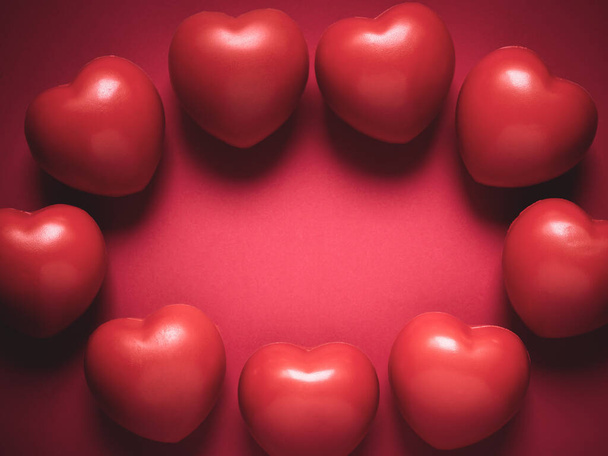 Rote Herzen auf rotem Hintergrund mit Kopierraum. Kranz aus vielen roten Kugelschaumstoff mit Herzform. Liebe, Pflege und Valentinstag runden Grenzkonzept ab. - Foto, Bild
