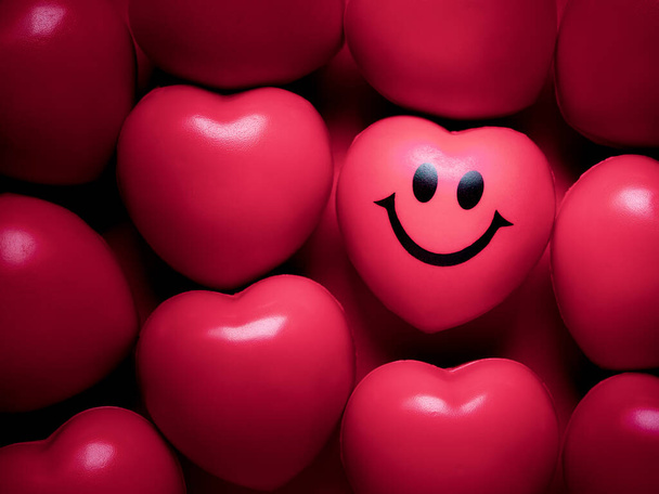 Червовый фон. Розовое сердце со счастливым и улыбающимся лицом среди множества сладких розовых шариков с формой сердца. Любовь, забота и День святого Валентина
. - Фото, изображение