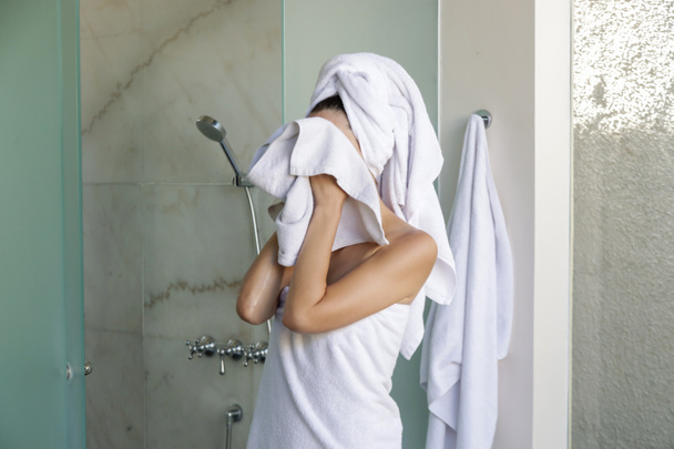 Young caucasian woman wrapped in towels walking out shower cabin  - Фото, изображение
