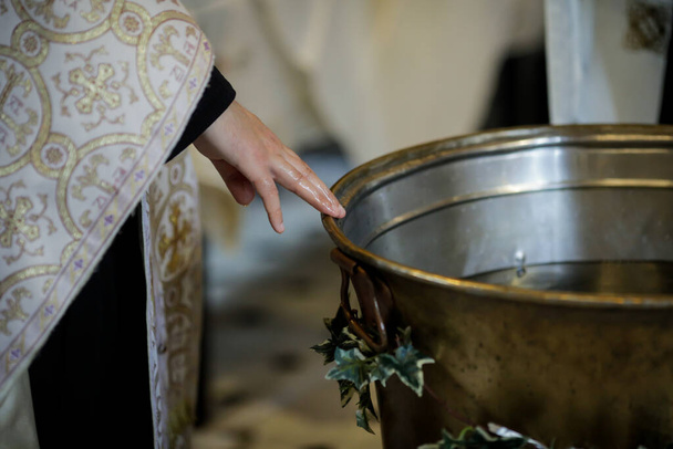 Bukareszt, Rumunia - 24 maja 2020 r.: Szczegóły ręką ortodoksyjnego księdza testującego ciepło wody w chrzcielnicy. - Zdjęcie, obraz