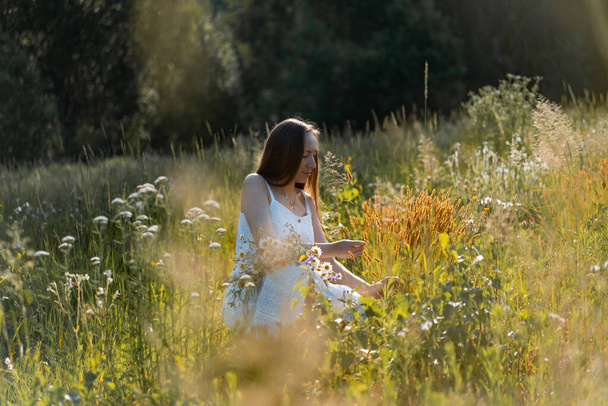 young beautiful woman with long hair in a white dress and hat among the yellow field of rye and wheat. - Photo, image