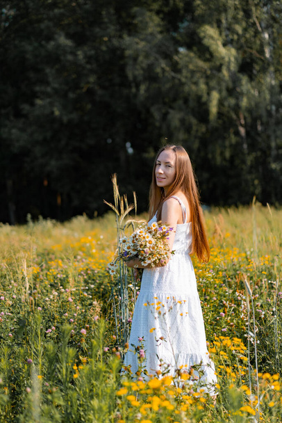 fiatal gyönyörű nő hosszú haj egy fehér ruha és kalap között a sárga mező rozs és búza. - Fotó, kép