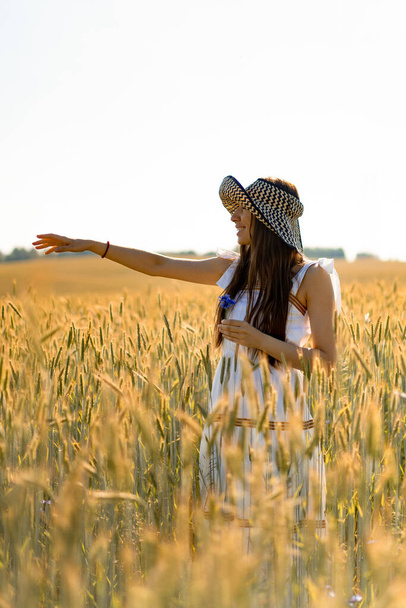 young beautiful woman with long hair in a white dress and hat among the yellow field of rye and wheat. - Zdjęcie, obraz