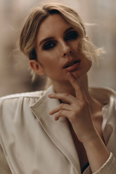 Fashionable portrait of a stylish blonde woman in elegant totall beige look leather trench coat and smoky eyes makeup in the outdoor. Spring - autumn fashion concept. Soft selective focus. - Foto, imagen