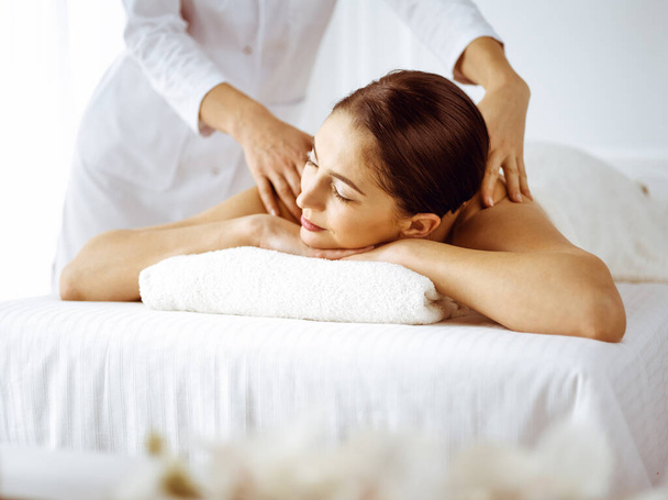Beautiful brunette woman enjoying back massage with closed eyes. Spa and medicine concept - Fotoğraf, Görsel