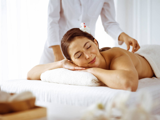 Beautiful brunette woman enjoying back massage with closed eyes. Spa and medicine concept - Photo, Image