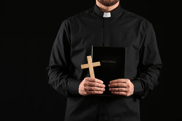 Young priest with Bible on dark background - Foto, afbeelding