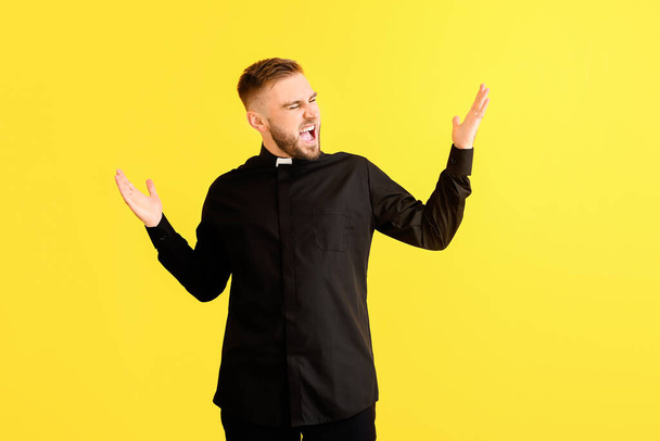 Angry young priest on color background - Photo, Image